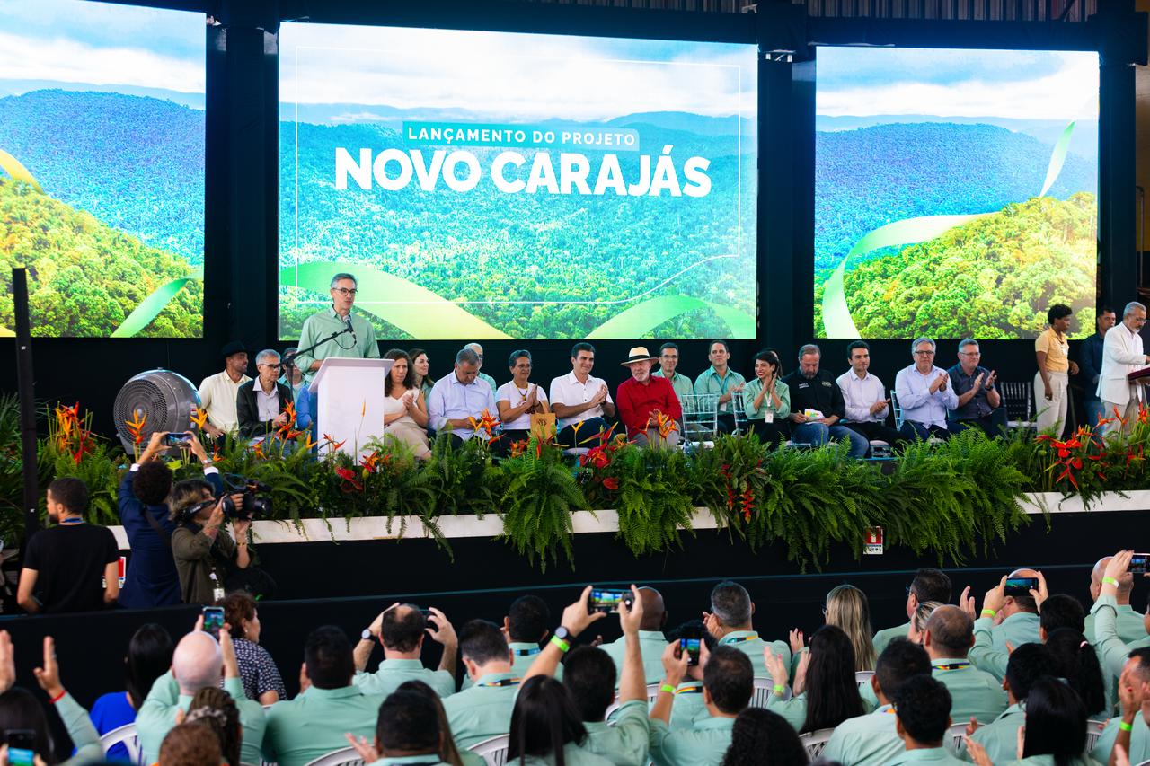 Grupo de pessoas assiste a executivos da Vale apresentarem ideias em um palco com imagem escrita Nova Carajás