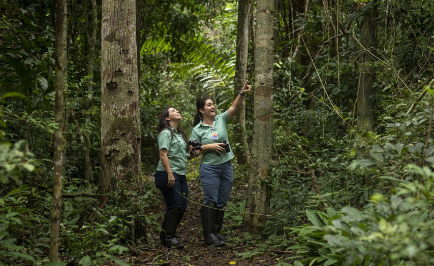 duas funcionárias da Vale vestidas de verde centralizadas em mata verde