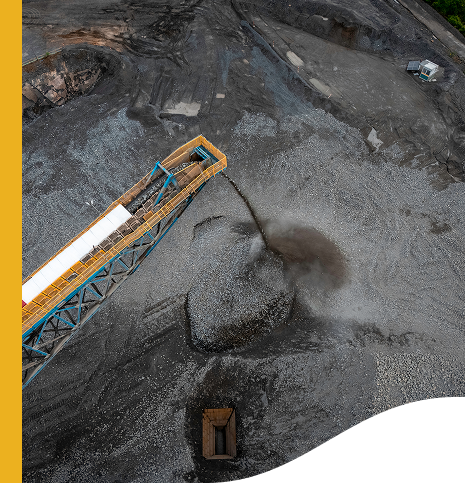 Aerial image of a mining or construction site, with a conveyor belt system transporting and depositing gravel or similar material onto a large pile.