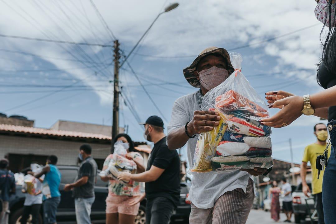Man in a street, with a mask on, donating food to a woman. They are surrounded by people also receiving donations.