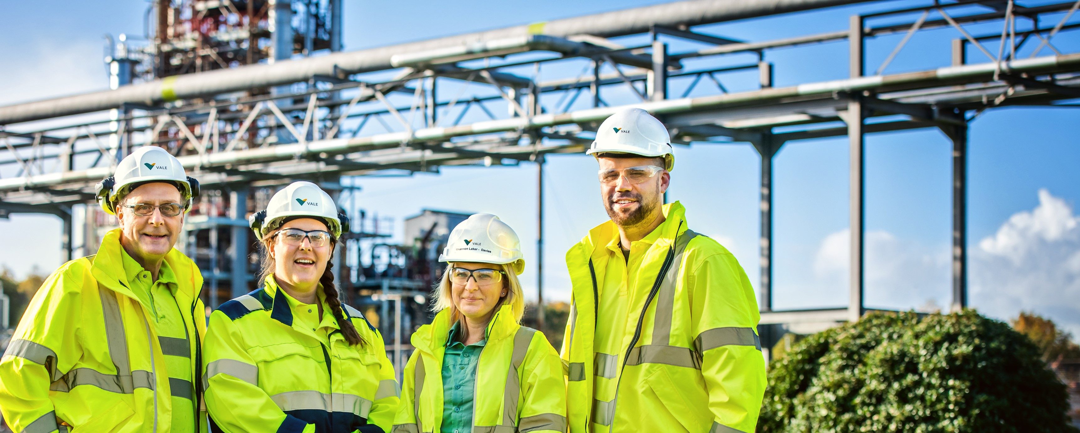 Four Vale employees, two men and two women, are smiling for the photo. They are wearing florescent protective clothing, helmets and goggles