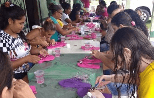 At a table, several women produce handcrafted slippers.