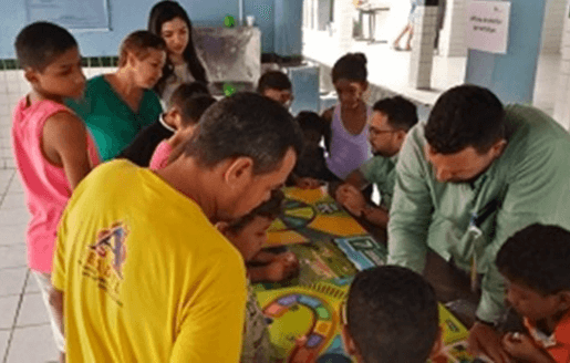 A group of adults and children lean over a table where there is a kind of map.