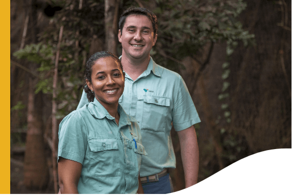 Foto de um homem e uma mulher sorrindo. A mulher é negra e está de cabelo preso, o homem é branco e tem cabelo curto. Os dois estão usando uniforme, camisa verde de botões com logo da Vale e calça jeans.