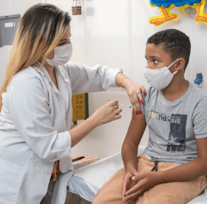 Photo of a healthcare professional holding a child's arm with one hand and applying an injection with the other. Both are wearing face masks.