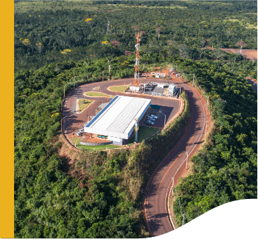 In a place surrounded by trees, there is a large shed and a power tower, as well as a road.