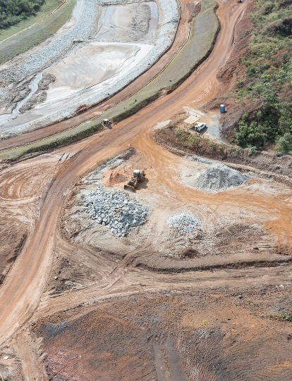 Foto de uma obra para eliminação de barragem com caminhões, terra, vegetação
