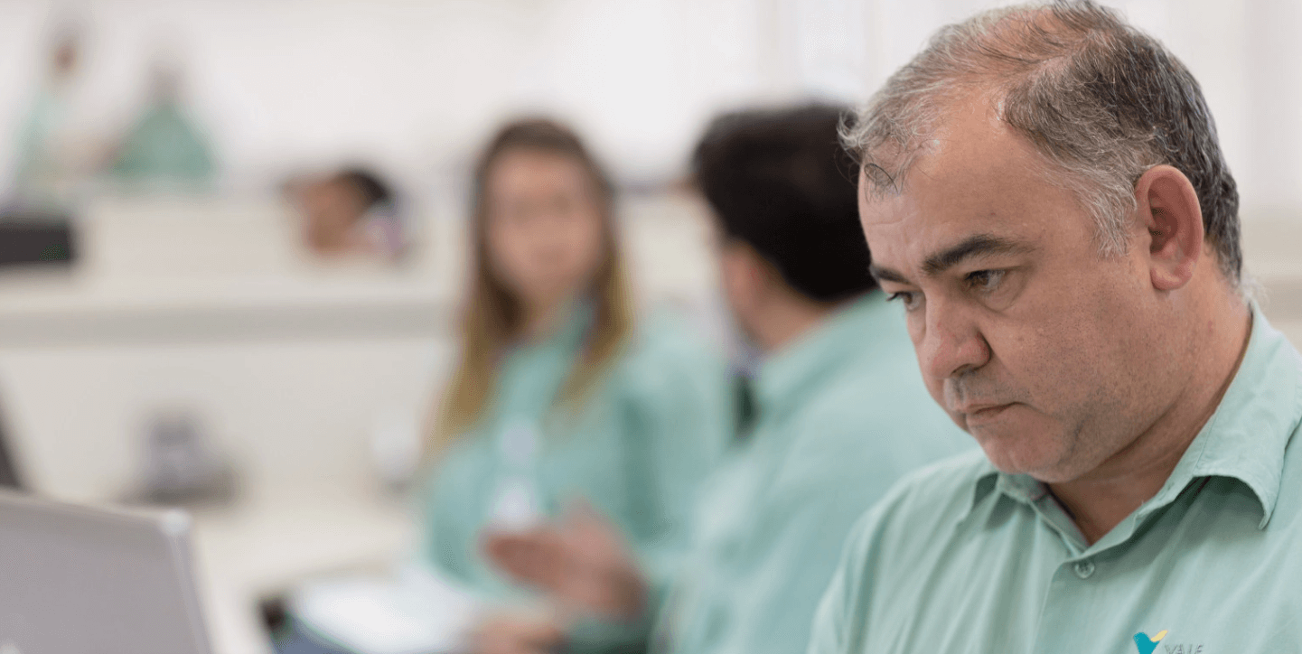 Gray-haired Vale employee, with a serious expression. He is wearing a green shirt with the Vale symbol.