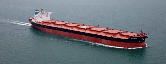 Imagem de um navio cargueiro de grande porte. Ele é vermelho e tem uma faixa preta e está navegando em alto mar.
