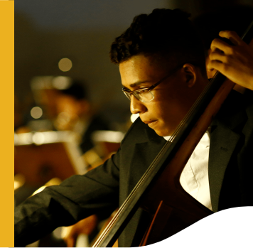 Jovem, de óculos, tocando um instrumento musical. Ele está de roupa social.