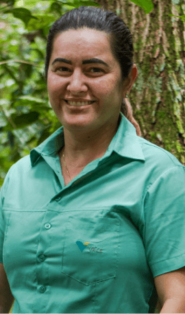 A women smiling in an area with trees. She is wearing a light green shirt and her hair back.