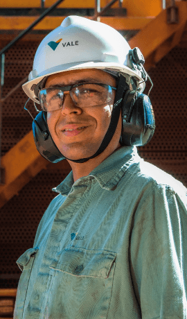 Photo of a man smiling. He is wearing a green Vale button-down shirt, ear protection, a helmet and goggles