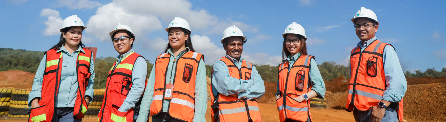 A group of Vale employees in an open area. They are wearing vests, uniforms and protective hats.