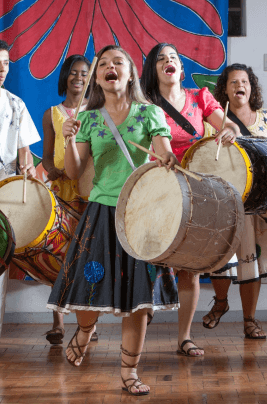 Várias jovens tocando tambores e cantando.