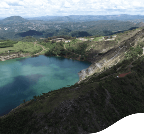 Foto tirada de cima de um espaço com rochas, plantas e um grande lago.