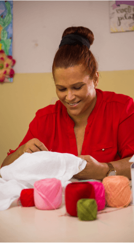 A woman is embroidering a white cloth and there are several colored threads in front of her.