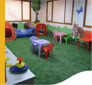 A closed room with synthetic grass and illustrations of animal on the walls. There are children's toys in the place.