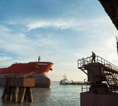 Image of a port where a ship is docked, and in the right corner of the photo, there is a man on top of a metal structure of the operation, wearing Vale uniform.