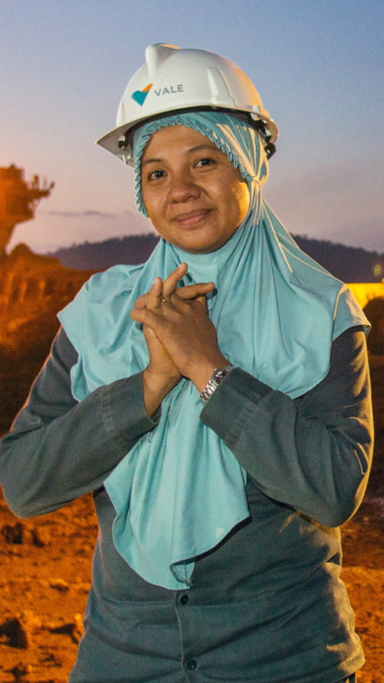 Seorang wanita yang lembut dengan helm, hijab dan baju terusan Vale dengan tangan disilangkan di depan dada berpose untuk berfoto.