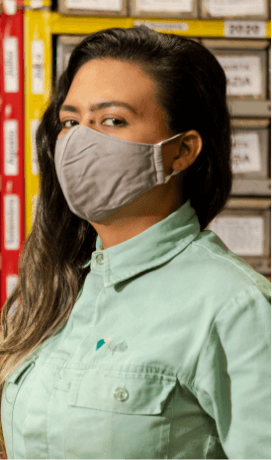 Photo of a woman taken from the chest up. She is looking straight into the camera, with her hair down, wearing a light green shirt with Vale logo and a face mask.