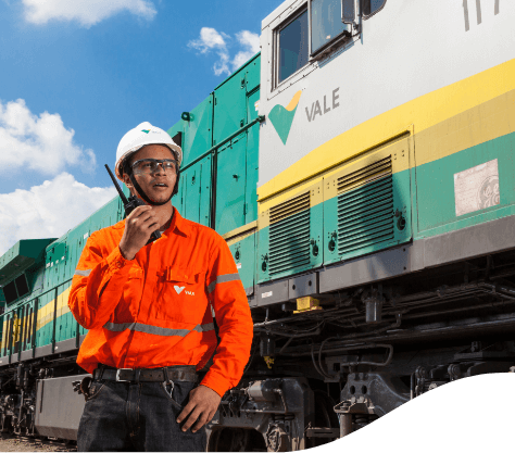 Vale employee, using a radio transmitter. He's in front of a train, wearing an orange uniform, helmet and goggles.