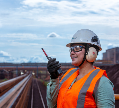 A Vale employee, in uniform and protective gear, smiles for a photograph. She is in an operational environment.