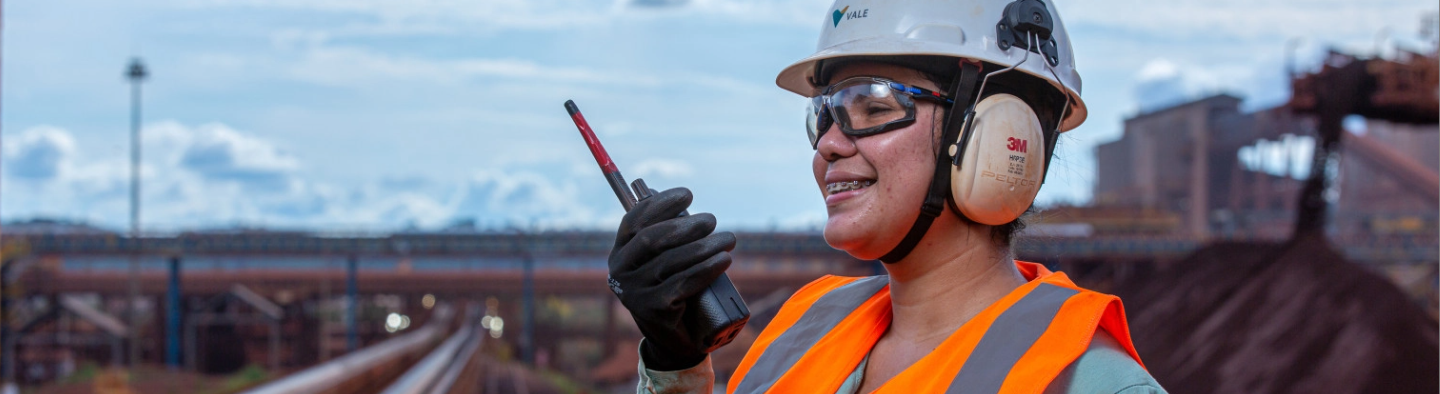 A Vale employee, in uniform and protective gear, smiles for a photograph. She is in an operational environment.