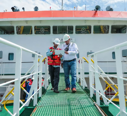 Two men were walking along a footbridge connected to a ship. They both looked at a piece of paper in the hand of one of the men.