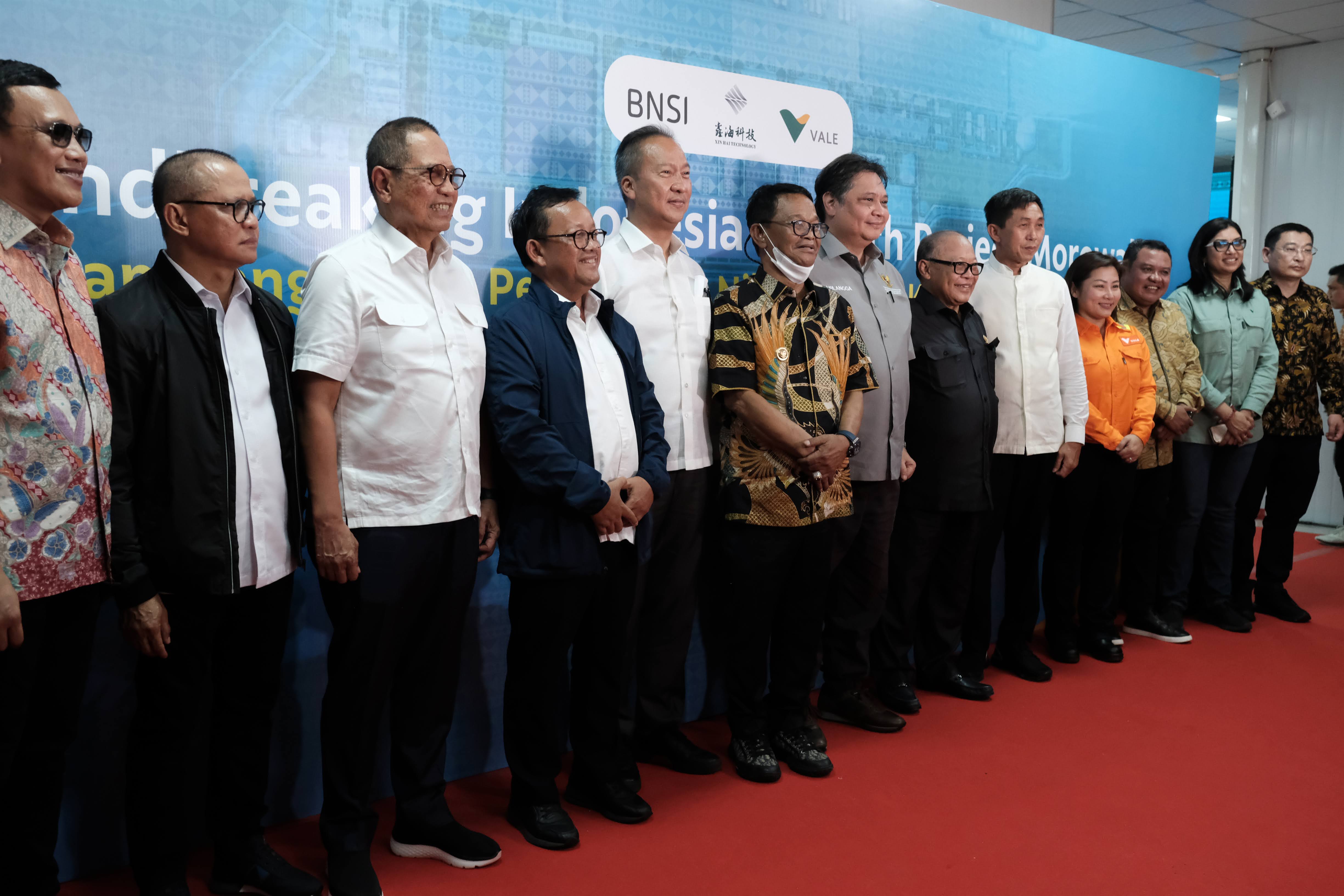 Photo of eleven men and two women wearing business clothes in front of a banner with the logo of Vale and other companies