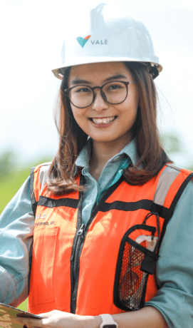 A woman with prescription glasses, medium straight hair, Vale uniform, and protective equipment holds a clipboard and smiles for a photo.