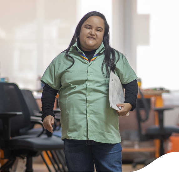 A disabled woman is holding a briefcase under her arm and smiling for a photo. She is wearing a Vale uniform.