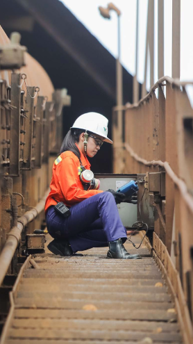 A woman is on some kind of bridge, handling equipment. She is wearing a Vale uniform, a hard hat and protective gloves and goggles.