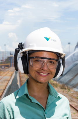 An employee, outdoors in an operation. She is wearing a helmet and goggles, smiling, and wearing a green uniform.