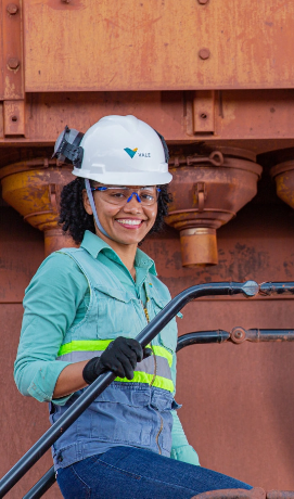 A Vale employee is climbing a ladder in an operation. She smiles for the photo and wears various protective equipment