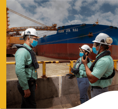 Three Vale employees are talking in front of a ship. All wear protective equipmentTrês empregado Vale estão conversando em frente a um navio. Todos usam equipamentos de proteção