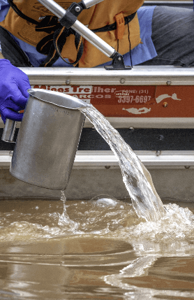 A person wearing gloves is taking water from a river.