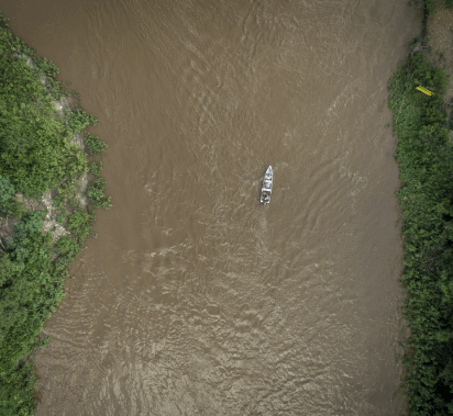 Aerial image of a river with turbid waters with a boat navigating. To the sides, there is dense vegetation.