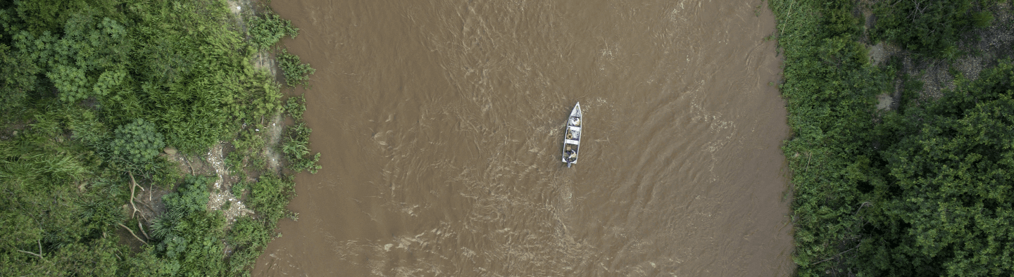 Aerial image of a river with turbid waters with a boat navigating. To the sides, there is dense vegetation.