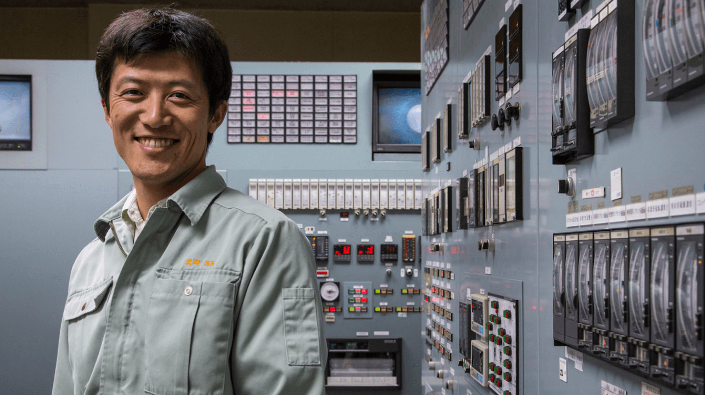 Um empregado Vale está sorrindo para foto. Atrás dele há uma sala de controle