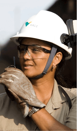 Photo of the face of Vale female employee. She is wearing a gray shirt, goggles, gloves and a white helmet with Vale logo.