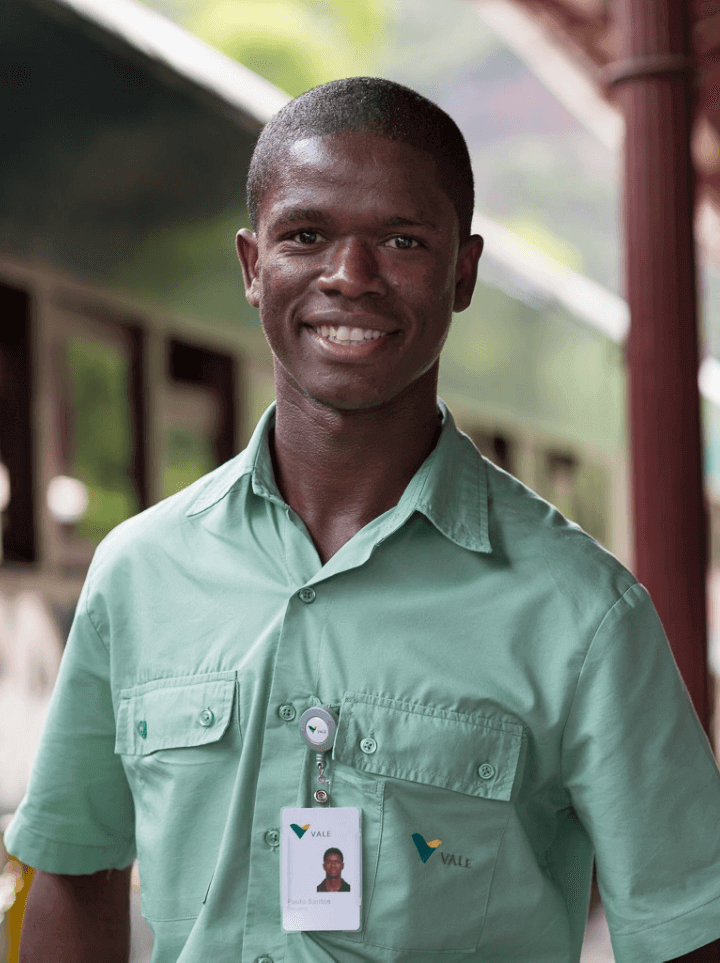 Homem negro de cabelos raspados sorrindo. Ele usa camisa verde com logotipo da Vale