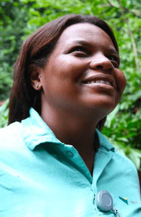 A female Vale employee looks at the horizon and smiles. She is out in the open, as you can see vegetation in the background.