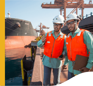 Two Vale employees are wearing protective vests and helmets in a port operation area.