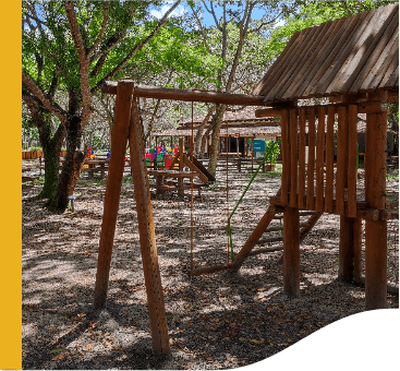 Outdoor children's playground. Toys, such as a scale and a slide, are made of wood. Some trees bring shade to the place.