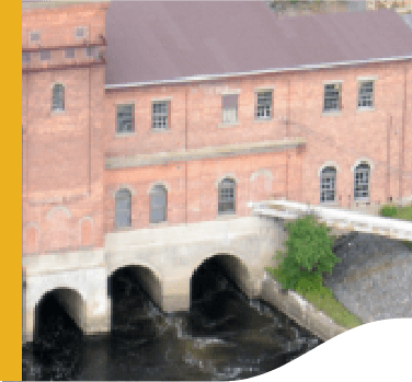 Photo of High Falls small hydropower plant. A shed structure with bricks and windows, and under the structure three water passages.