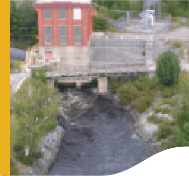 Foto de uma pequena central hidrelétrica de High Falls II. Uma estrutura com tijolos e janelas em uma ponte e embaixo um rio passando.