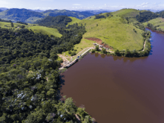 Foto de PCH Mello de cima, uma parte da foto com uma vegetação, montanhas e árvores e a outra com água