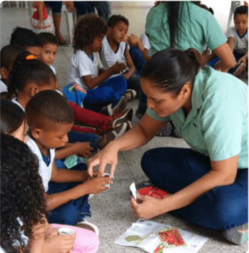 Several children are sitting on the floor, interacting with two Vale employees.