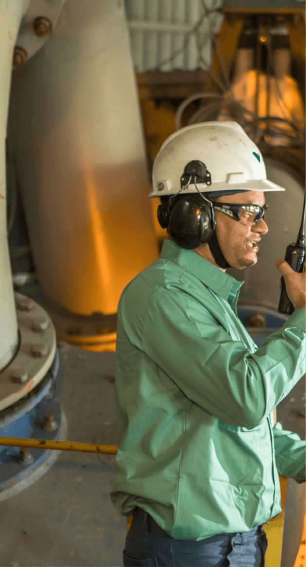 Belly to head shot of a man holding a radio in an operation. The man is wearing a Vale uniform, helmet, goggles, ear protection and a mask on his face.