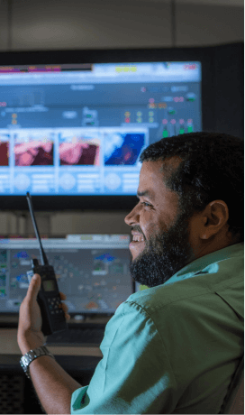 A bearded Vale employee is smiling and holding a radio transmitter. There are two monitors in the background.